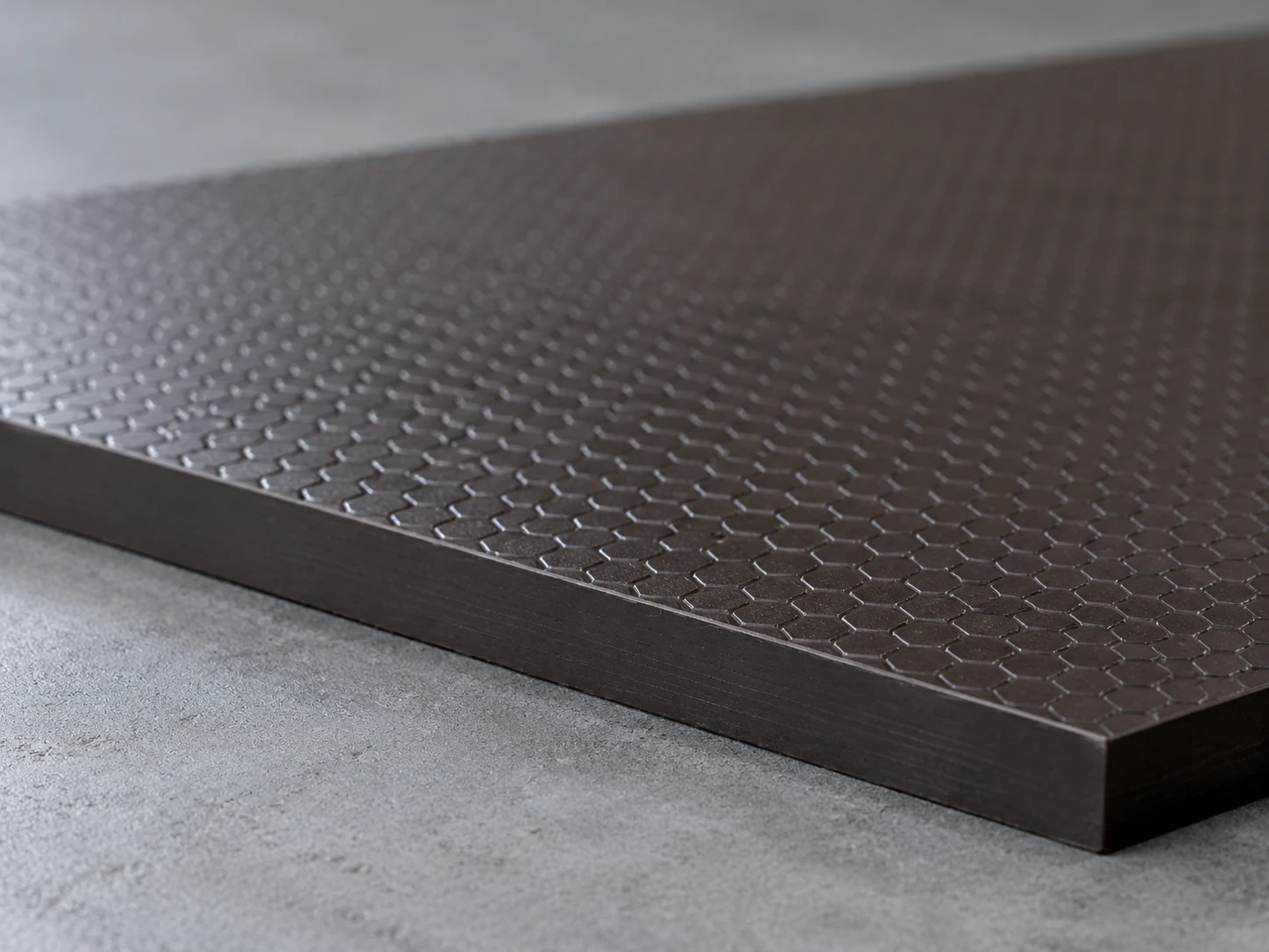 Low-angle close-up of anti-slip plywood: dark brown film with a raised hexagonal pattern and a sealed edge