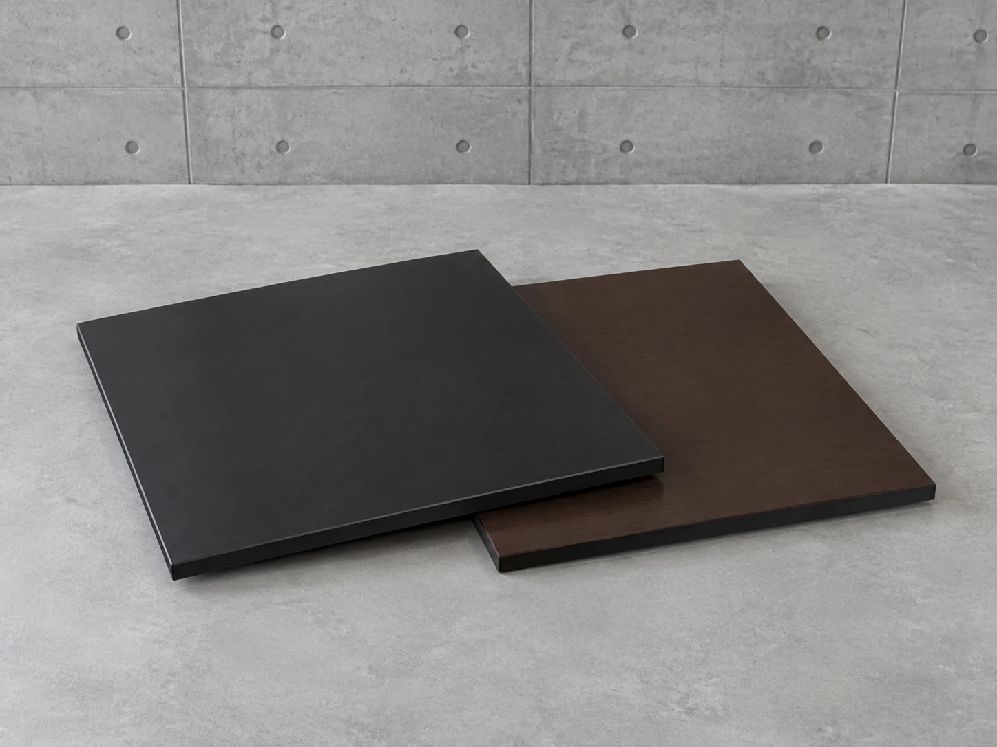 Two film-faced plywood panels overlapping on concrete, one with black film and one with dark brown film