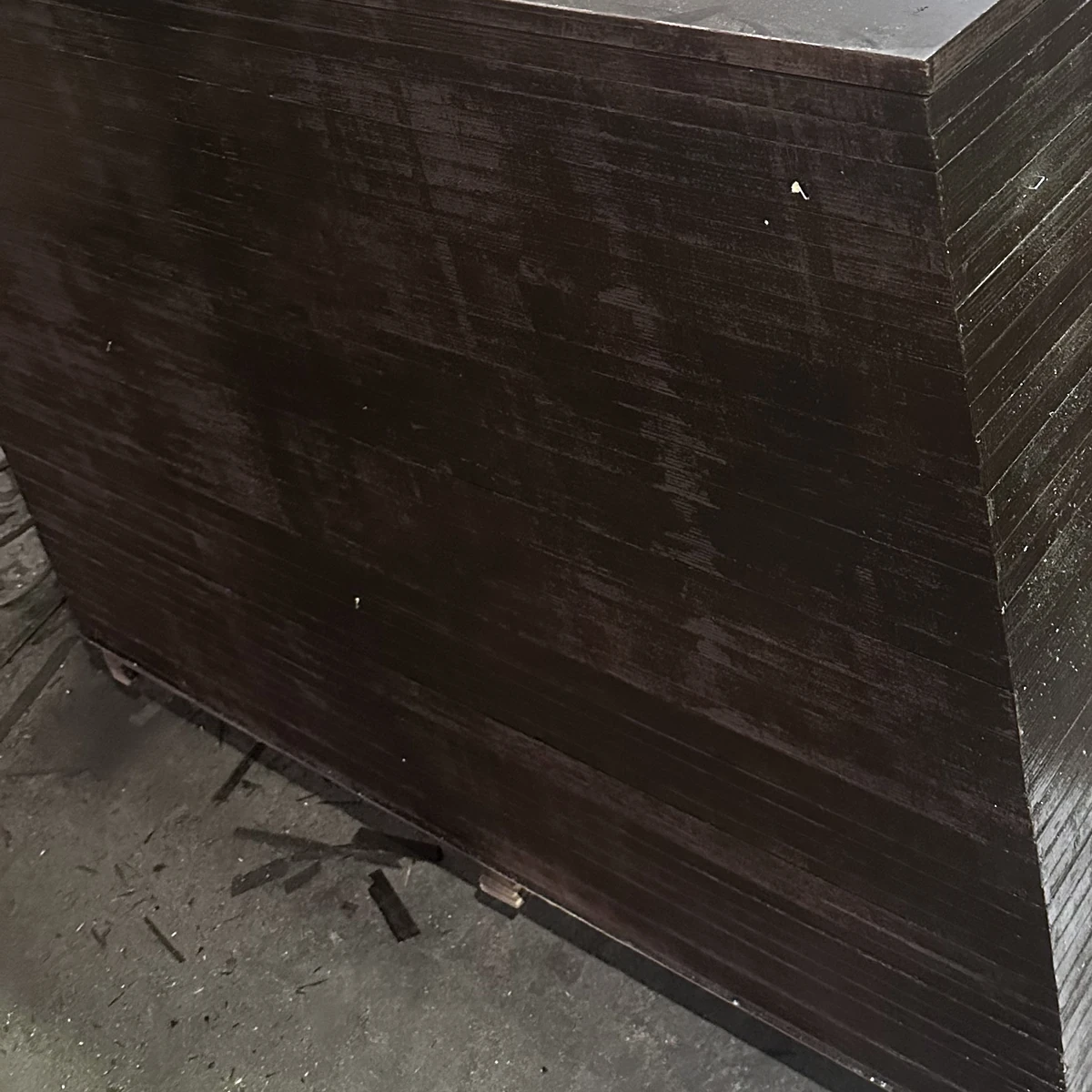 Side of a stack of film-faced plywood with dark sealed edges and the brown film top sheet