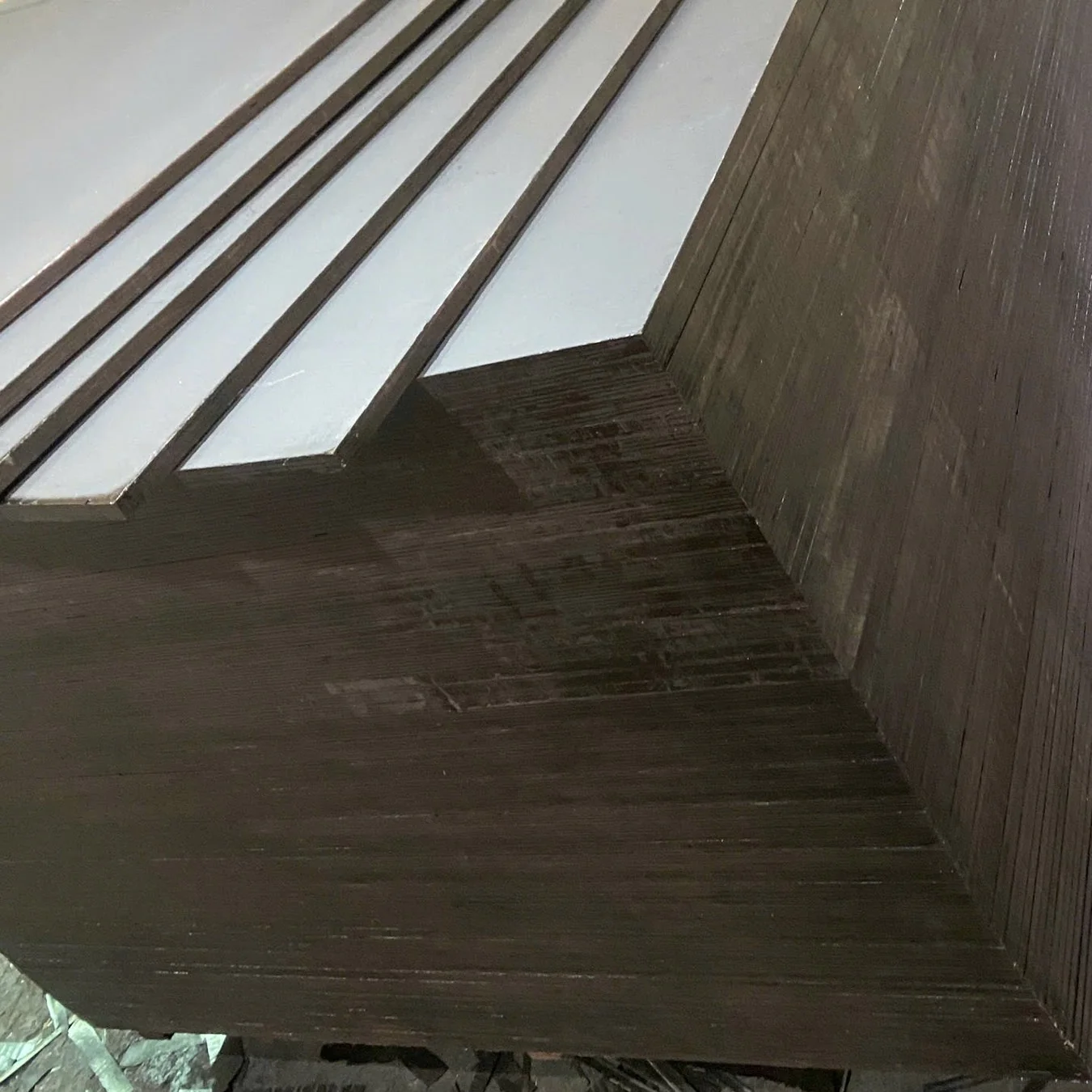 Film-faced plywood sheets fanned out in steps on a stack, showing film faces and dark edges