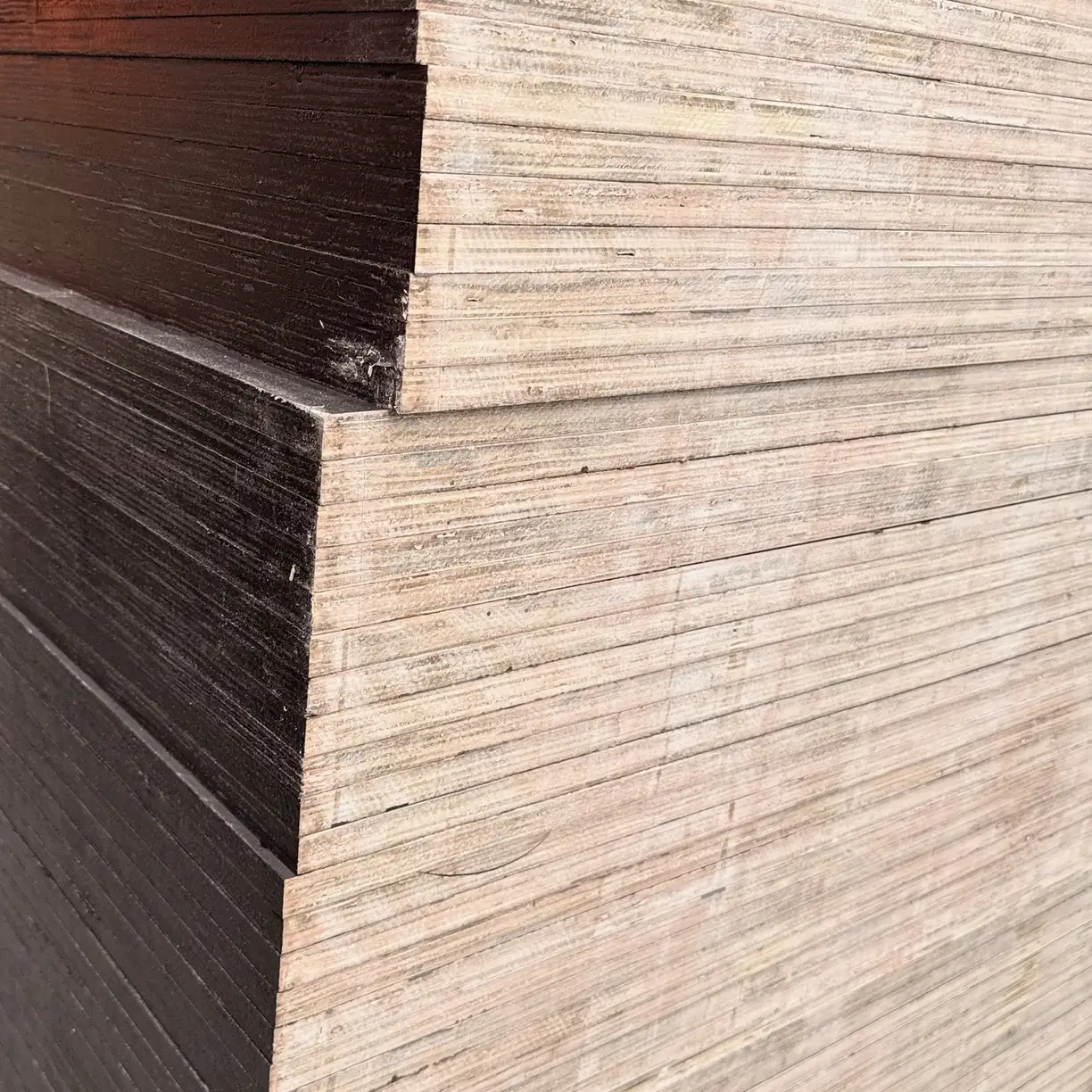 Stepped corner of a film-faced plywood stack with dark sealed edges beside natural multi-ply edges