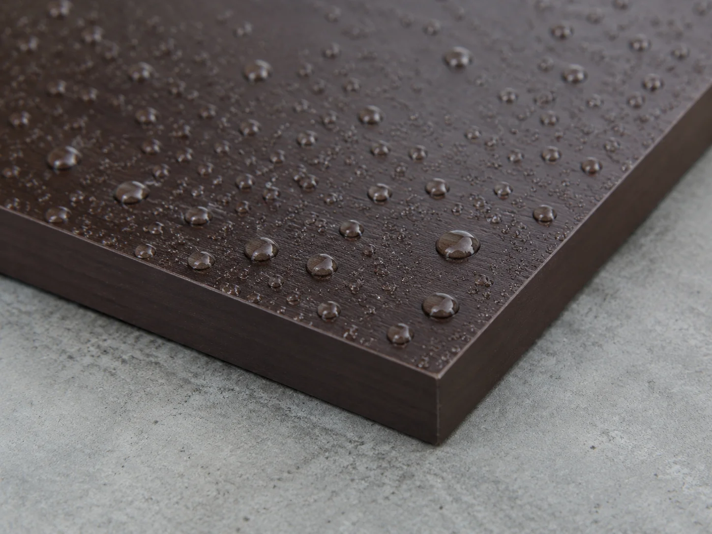 Water beading on the dark brown phenolic film of a plywood panel corner with a sealed edge